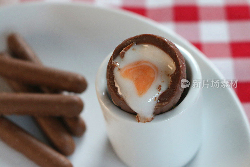 奶油/奶油蛋和巧克力手指饼干的形象在早餐桌上，蘸着甜奶油的复活节蛋黄和白色，红白格子桌布，甜点布丁糖果